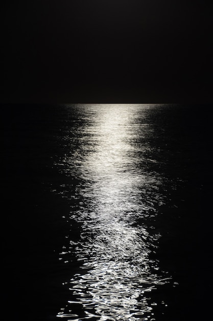 Reflexo brilhante da lua até o horizonte nas ondas do mar calmo em uma noite. Em preto e branco