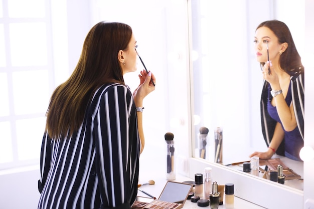 Reflexo da jovem bela mulher aplicando sua maquiagem olhando no espelho