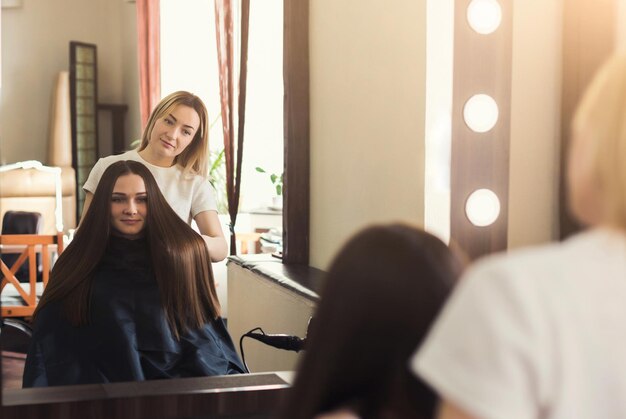 Reflexo de espelho de uma jovem mulher bonita discutindo penteado com o cabeleireiro