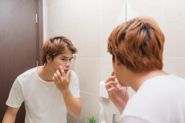 Reflexo de jovem no espelho verificando a barba por fazer no banheiro