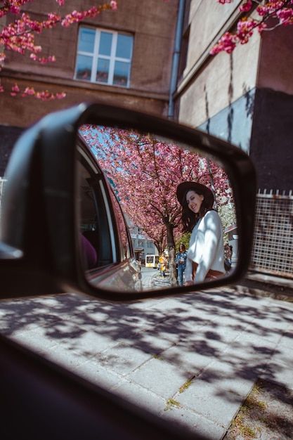 Reflexo de mulher sorridente no espelho traseiro do carro florescendo árvore de sakura no fundo a primavera está chegando