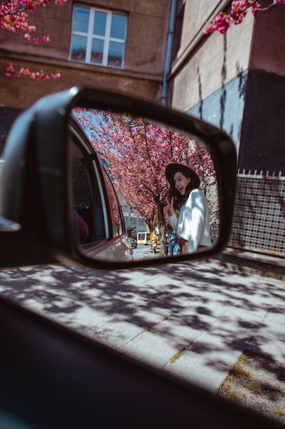 Reflexo de mulher sorridente no espelho traseiro do carro florescendo árvore de sakura no fundo