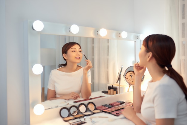 Reflexo de uma bela jovem aplicando sua maquiagem, olhando no espelho