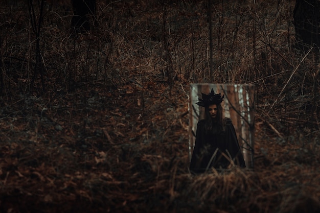 Foto reflexo de uma bruxa escura e assustadora em um espelho em uma floresta sombria