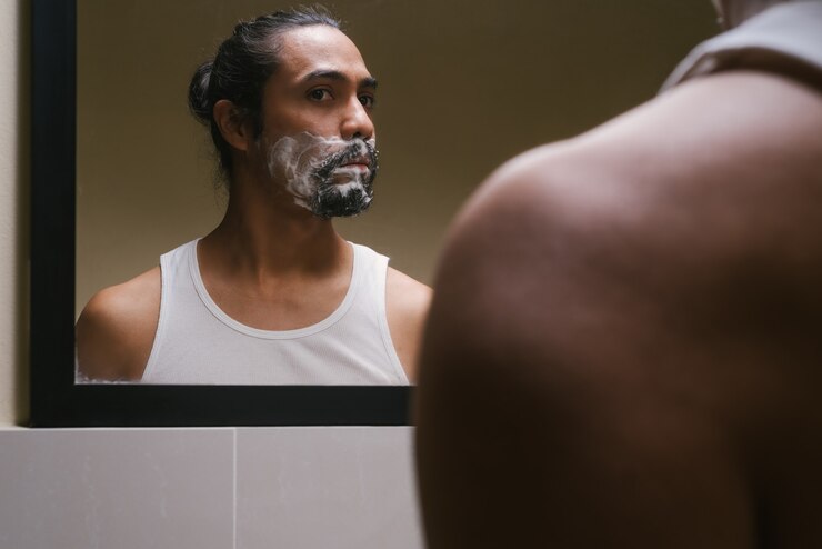 Foto reflexo no espelho do banheiro de um homem latino com creme de barbear