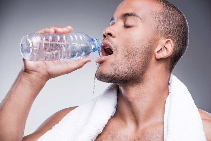 Foto refrescante após o treino. jovem africano sem camisa segurando uma garrafa com água e sorrindo
