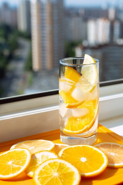 Refrescante bebida fría con hielo y rodajas de naranja en el fondo de la ciudad.