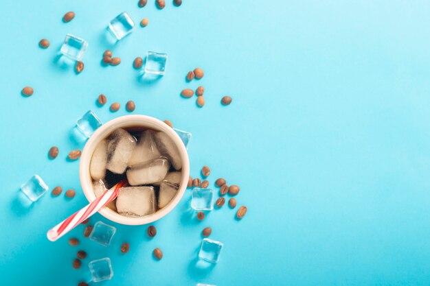 Refrescante café helado en un vaso y cubitos de hielo y granos de café sobre una superficie azul. Concepto de verano, cola con hielo, refrescante cóctel, sed. Vista plana, vista superior