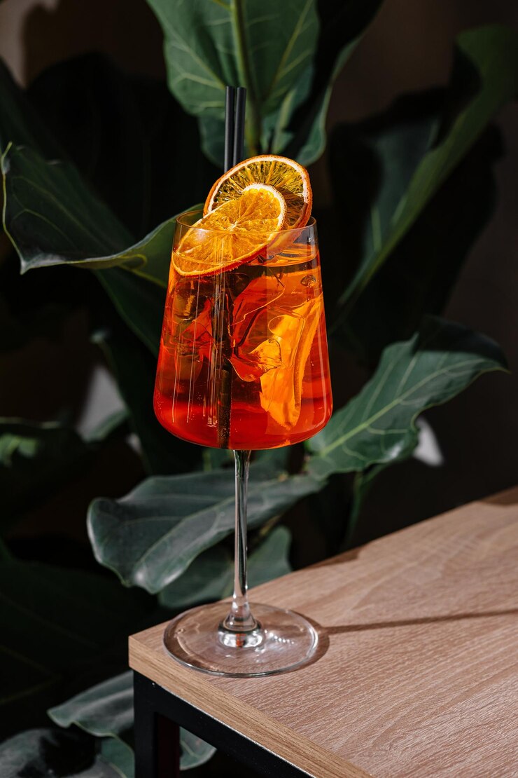 Refrescante cóctel de aperol spritz de pie en una mesa con plantas tropicales en el fondo