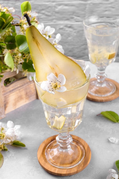 Refrescante coquetel de pêra em um copo decorado com frutas frescas e flores em fundo cinza claro Mocktail de verão