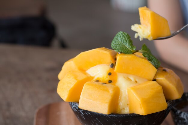 Refrescante helado de mango y fruta de la pasión en un tazón de cerámica en el escritorio de madera