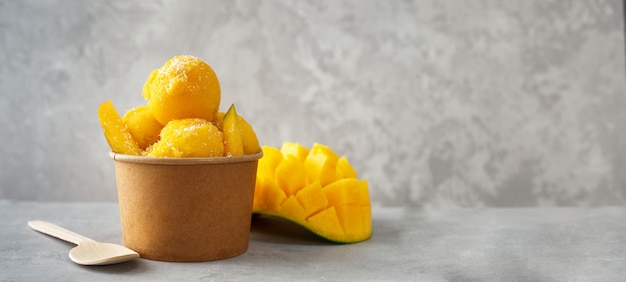 Refrescante helado de mango en una taza de papel artesanal sobre fondo gris