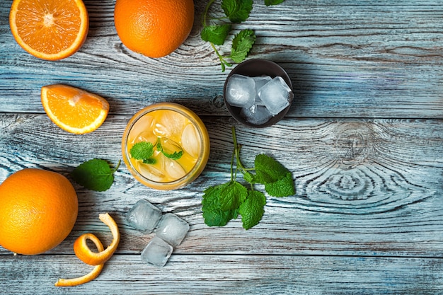 Refrescante jugo de naranja con menta y hielo sobre un escritorio gris azulado. Vista superior con espacio de copia.