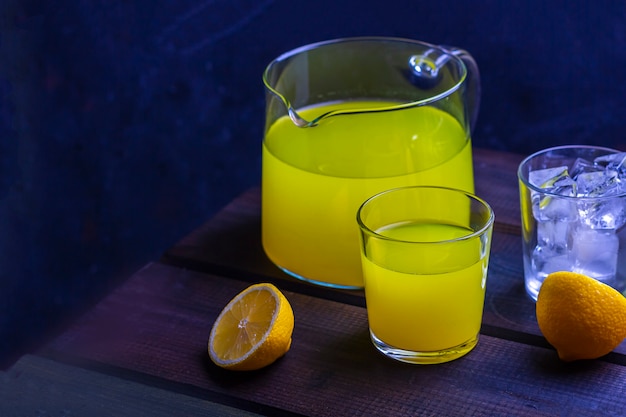 Refrescante limonada casera de cítricos en jarra y vaso sobre una mesa de madera