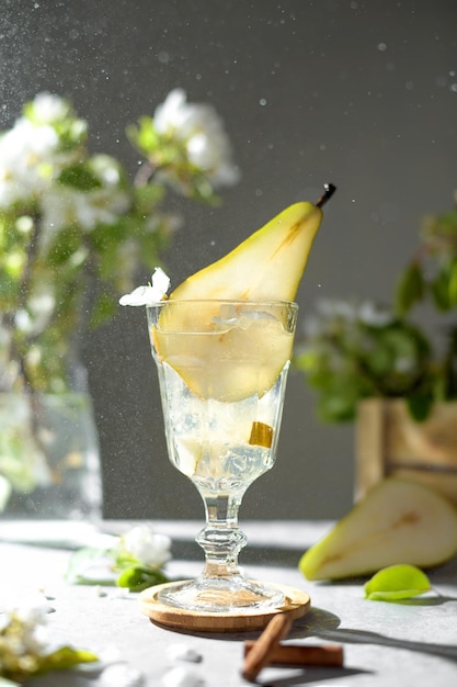 Refrescante limonada de coquetel de pêra em um copo com purê de pêra e frutas frescas e flores no fundo da mesa cinza claro