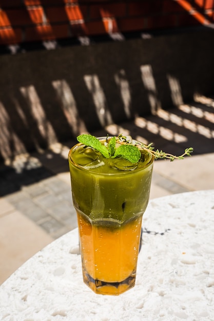 Refrescante matcha tónico helado con jugo de naranja en un vaso alto adornado con menta y tomillo