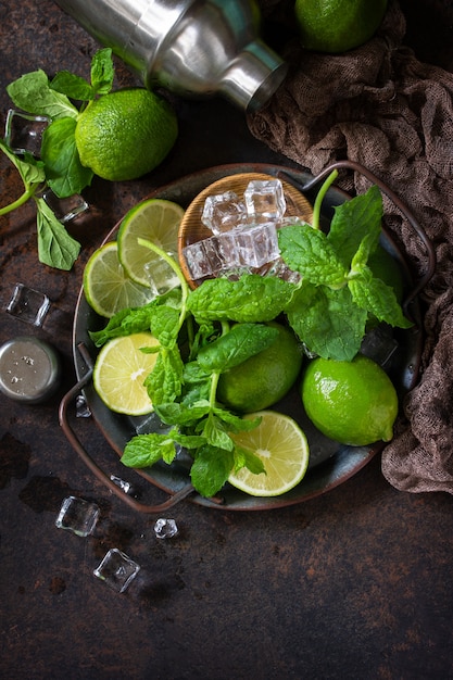 Refrescante preparación de cóctel Mojito. Menta, lima, ingredientes de hielo y utensilios de bar sobre un fondo de piedra oscura Copie el espacio.