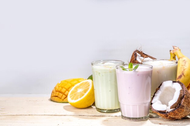 Refrescantes batidos de yogur o batidos Tres vasos con batidos de frutas Plátano blanco manzana verde aguacate batido de frutas tropicales de mango amarillo En mesa de madera blanca copia espacio