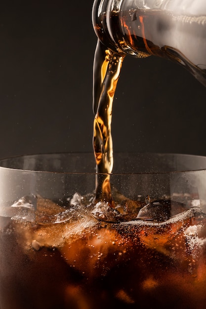 El refresco gaseoso gaseoso se vierte en un vaso de una botella. Hermosa textura de primer plano de hielo y burbujas en un vaso de espuma