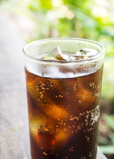 Refresco negro en vidrio. Vista al jardín con bokeh