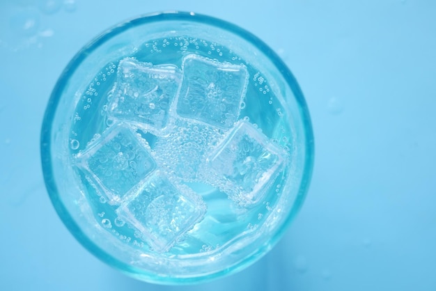 Refrescos en un vaso con cubitos de hielo sobre fondo azul.