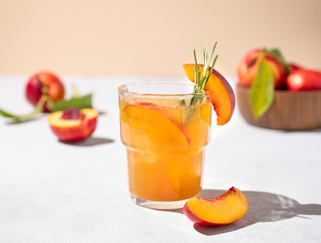 Refrigerante chá de pêssego com gelo e romário Bebida vegetariana fria e saudável caseira em um fundo claro com frutas frescas e sombras