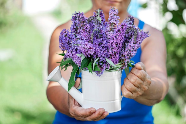 Regadera con flores en manos de una anciana, primer plano