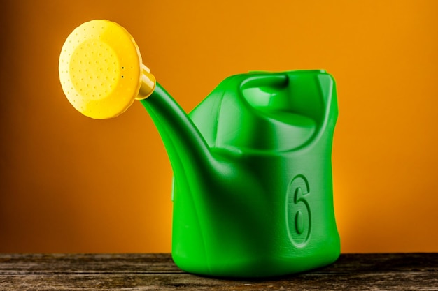 Regadera de plástico verde sobre una mesa de madera sobre un fondo amarillo