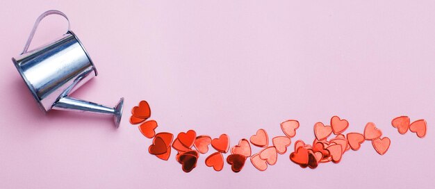 Foto regadera de plata flores vertiendo corazones sobre fondo rosa fondo de san valentín