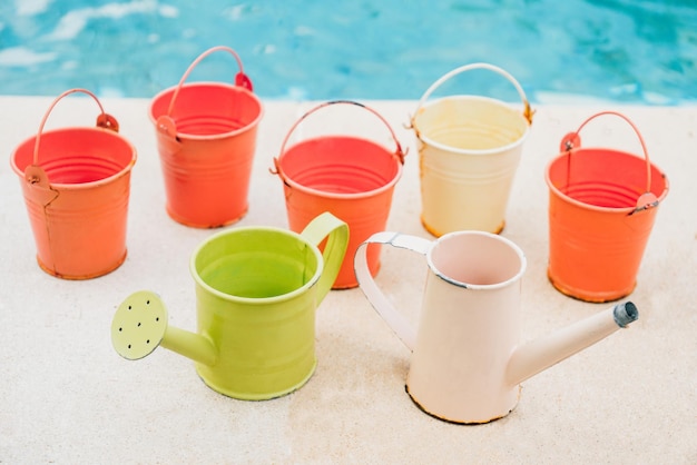 Regaderas de colores y baldes para plantas en el jardín cerca de la piscina