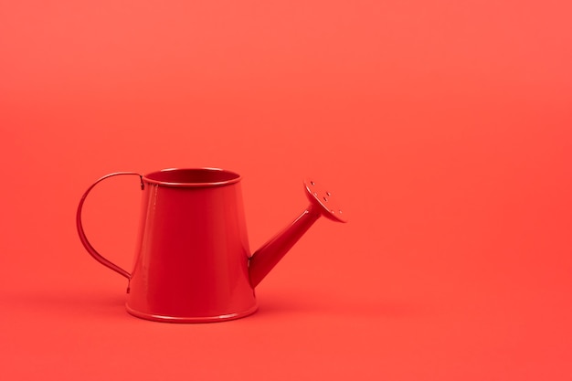 Regador vermelho em uma parede vermelha. Foto minimalista com espaço de cópia para seu texto