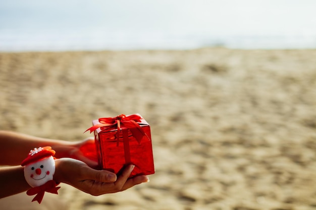 Regalo de año nuevo en caja roja en mano en la playa en los trópicos