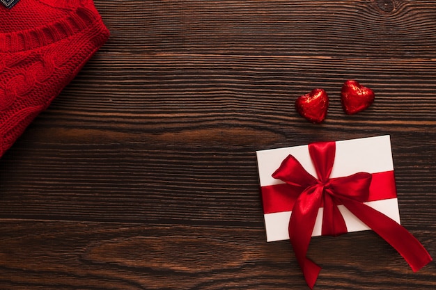 Regalo blanco con una cinta roja y dos corazones rojos chocolate aislados sobre un fondo de madera oscura. Vista lateral superior de un flatlay cálido de celebración. Día de San Valentín y concepto de Navidad. Copyspace.