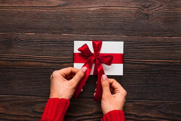 Regalo blanco con una cinta roja en manos de mujer sobre un fondo de madera oscura. Concepto de día de San Valentín. Copyspace.