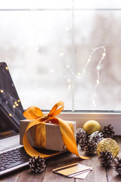 Regalo con una cinta dorada y una computadora portátil y una tarjeta bancaria en una mesa de madera Compras en línea de Navidad