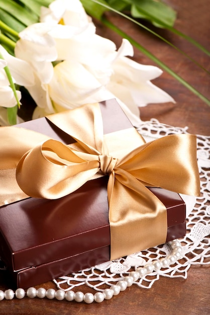 El regalo con una cinta dorada y un ramo de tulipanes blancos con hojas verdes puede usarse como postal