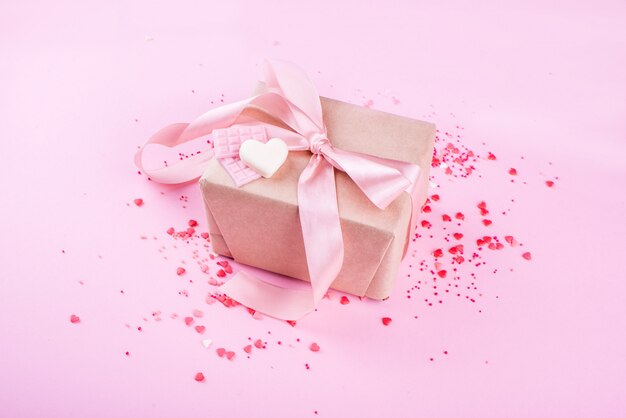 Regalo con cinta de raso con pequeñas rosas sobre un fondo rosa. Corazones, contenido festivo. Día de San Valentín.