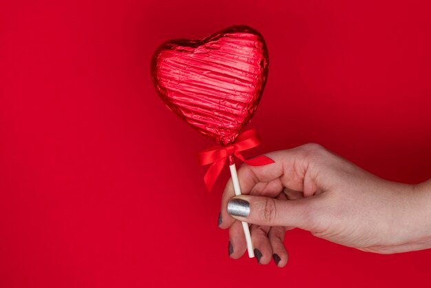 Regalo del día de San Valentín Mano femenina sosteniendo un loll en forma de corazón sobre un fondo rojo.