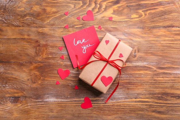 Regalo para el día de San Valentín, tarjeta y corazones rojos en madera