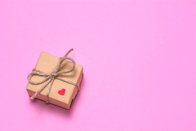 Un regalo envuelto en papel kraft sobre un fondo rosa Corazón rojo de papel en una caja de regalo