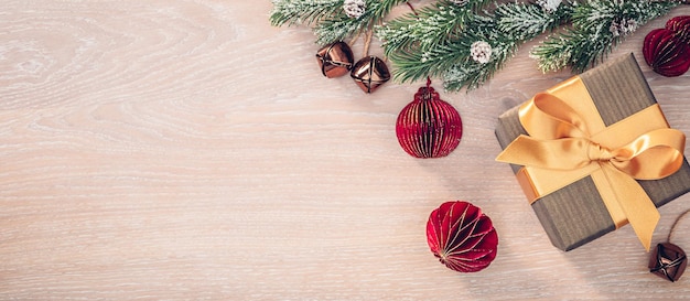 Regalo con lazo de cinta dorada rama de árbol de navidad y adornos sobre fondo de madera clara