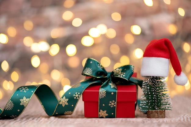 Regalo de Navidad y arbolito de Navidad con sombrero de Papá Noel en un fondo con luces brillantes