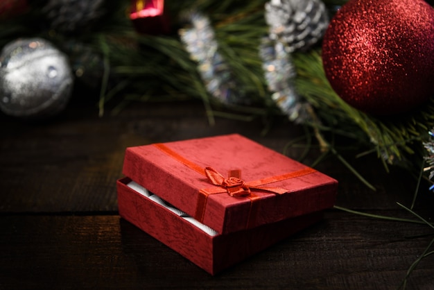 Regalo de Navidad en caja roja con cinta roja sobre fondo de madera, rodeado por una corona de Navidad