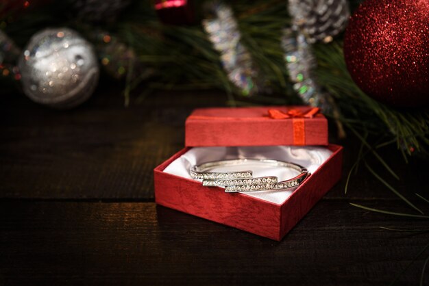Regalo de Navidad en caja roja con cinta roja sobre fondo de madera, rodeado por una corona de Navidad
