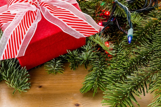 Regalo de Navidad en caja roja en ramas de hoja perenne vivas.