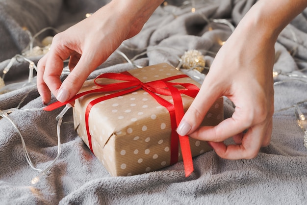 Regalo de Navidad envuelto en papel de lunares con cinta roja, manos femeninas sosteniendo cintas