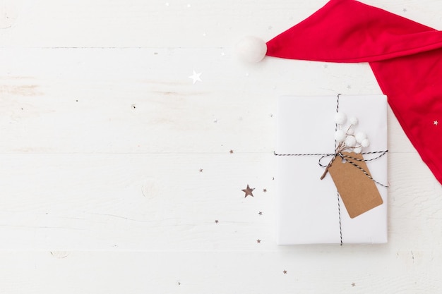 Regalo de Navidad envuelto en papel de regalo blanco Adornos navideños en el sombrero de Papá Noel sobre fondo de madera