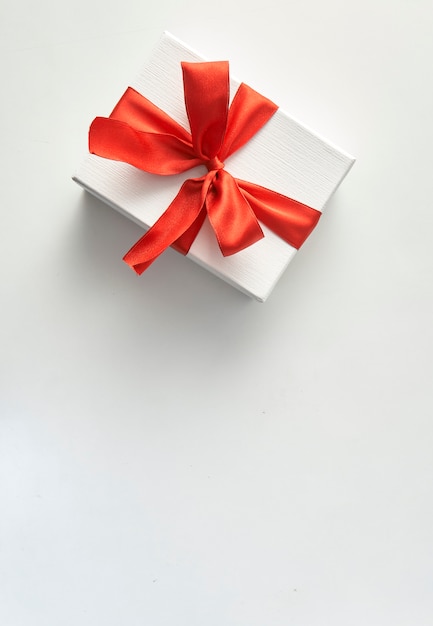 Un regalo de navidad en papel de regalo blanco y cintas rojas.
