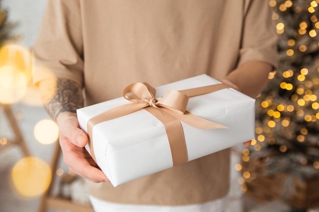 un regalo de Navidad en un paquete blanco con un lazo en sus manos