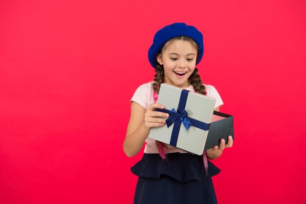 Regalo de Navidad para su hija Una niña pequeña y linda recibió un regalo navideño Los mejores regalos de Navidad Un niño emocionado por desempacar su regalo Una niña pequeña sostiene una caja de regalo con una cinta sobre fondo rojo